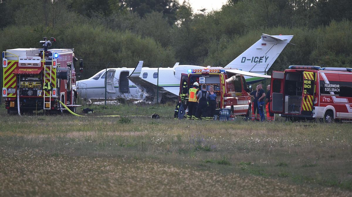 Einsätzkräfte der Feuerfehr stehen vor dem Kleinjet, der nach der Landung auf dem Flugplatz hinter dem Maschendrahtzaun in einem Feld liegt. Foto: Mahnke/dpa
