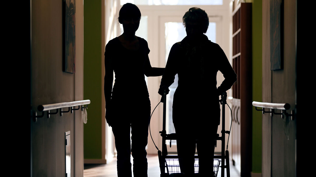 Eine Pflegekraft (l.) begleitet die Bewohnerin eines Altenheims mit Rollator beim Gang über den Flur. Foto: dpa/Oliver Berg