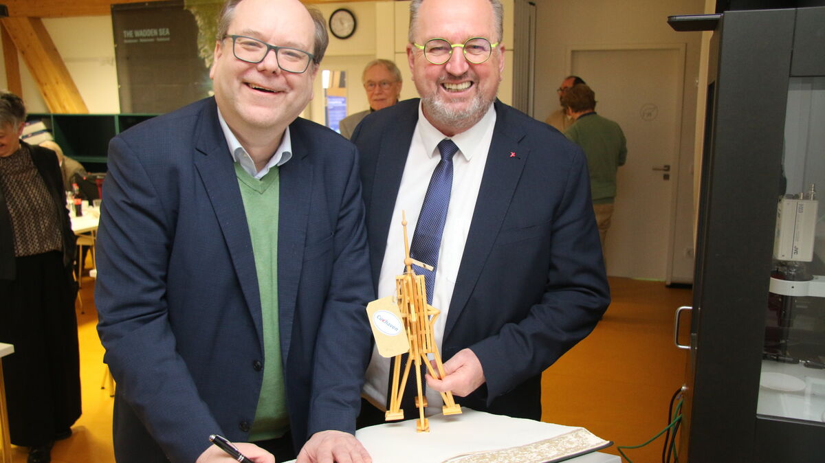 Symbolischer Moment im WattBz: Umweltminister Christian Meyer trägt sich ins Gästebuch der Stadt Cuxhaven ein, während Oberbürgermeister Uwe Santjer (SPD) ihm eine handgefertigte Holzkugelbake überreicht – ein Wahrzeichen der Stadt, hergestellt von Menschen der Lebenshilfe Cuxhaven. Foto: Potschka