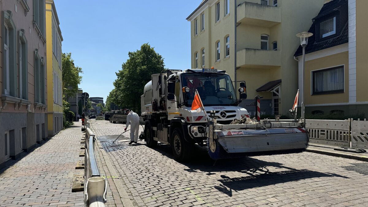 Ein Arbeiter im weißen Schutzanzug trägt auf das Kopfsteinpflaster der Friedrich-Carl-Straße eine Emulsion aus Bitumen auf. Foto: Keck