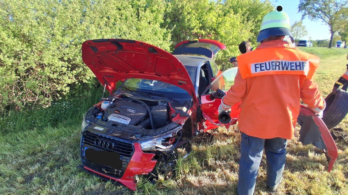 Der Audi kommt stark beschädigt auf einer Wiese zum Stehen. Feuerwehrkräfte sammeln Trümmerteile zusammen. Foto: Lange