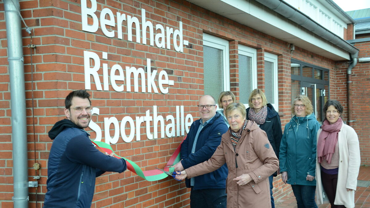 Anneliese Riemke durchschnitt gemeinsam mit Samtgemeindebürgermeister Frank Springer (l.) und dem TSV-Vorsitzenden Andreas Wehber im Beisein der Töchter von Bernhard Riemke sowie der Übungsleiterin Tanja Söhl (r.) das Band zur Umbenennung der Lamstedter Sporthalle. Foto: Rohde