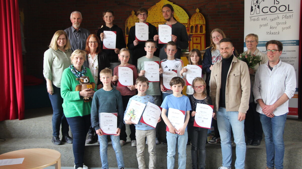 Die (noch anwesenden) drei Bestplatzierten der vier Altersgruppen und die Jury versammeln sich gemeinsam mit Schulleiterin Gudrun Neumann zum Abschlussfoto beim Kreisentscheid des Plattdeutschen Lesewettbewerbs in der Grundschule Cadenberge. Foto: Grewe