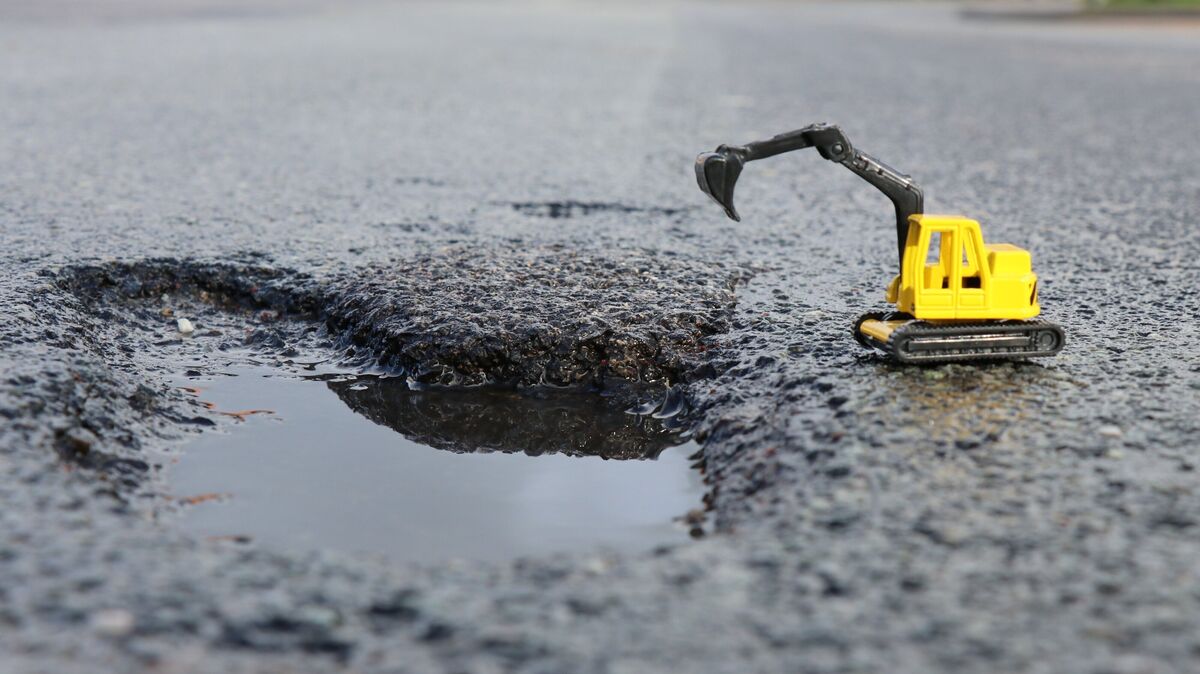 Ein Miniaturbagger steht symbolisch am Rand eines Schlaglochs, das nach dem harten Winter auf der Landesstraße 117 in Ihlienworth entstanden ist. Foto: Mangels