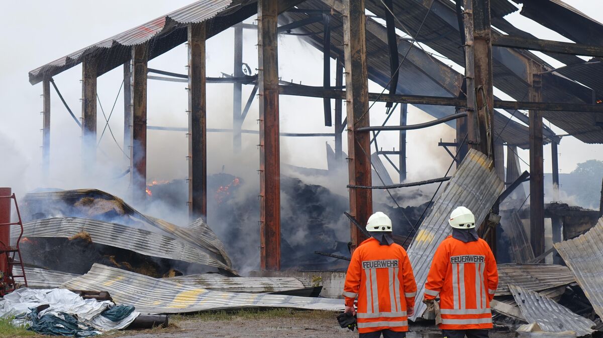 Zwei Feuerwehrmänner blicken auf die Halle, die schon während des Brandes in Schutt und Asche liegt. Foto: Kuczorra