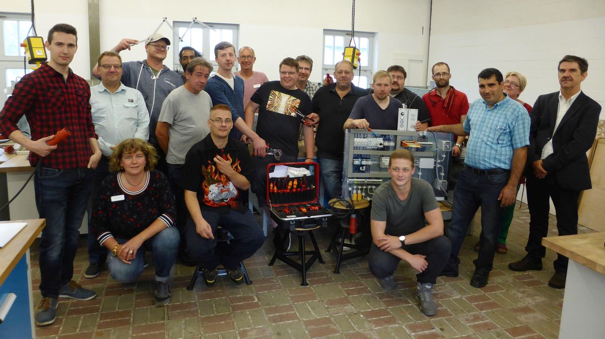15 frisch gebackene Industrieelektriker in ihrer Ausbildungswerkstatt mit BBW-Geschäftsführer Udo Heinsohn (ganz rechts), Projektleiterin Gudrun Zeschke (Zweite von rechts) und Ausbildern. Foto: von Allwörden