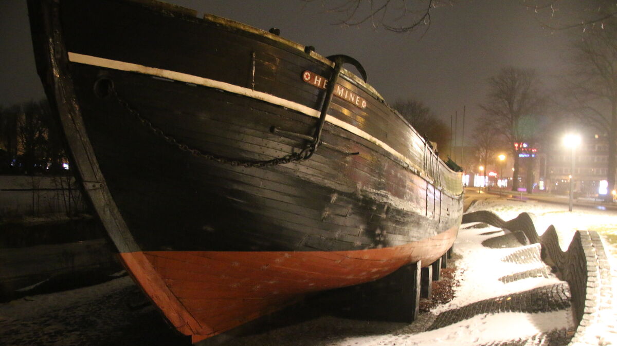 Trauriger Anblick mit Beleuchtung am Schleusenpriel: Die „Hermine" liegt im extra für sie gestalteten Umfeld im Schnee, ohne Masten und Takelage. Der Gaffelschoner ist zum Politikum geworden. Foto: Potschka