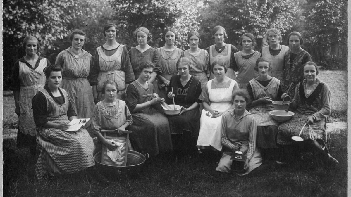 Die Aufnahme zeigt 18 Frauen eines ländlichen Hauswirtschaftskurses, die sich mit verschiedenen Arbeitsgeräten, darunter eine Kaffeemühle und ein Waschbrett, zum Gruppenbild versammelt haben. Das Foto wurde vermutlich um 1930 von einem Berufsfotografen angefertigt. Foto: Wilhelm-Heidsiek-Verlag