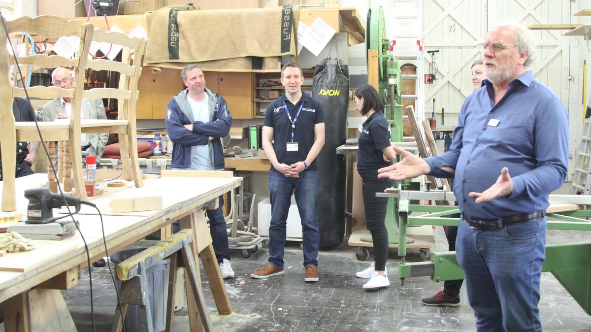 Norbert Struve (r.) in der Holzwerkstatt, in der wenig Vorgefertigtes zu finden ist, sondern wo stattdessen auf eigene Ideen gesetzt wird. Den Gästen entging der Boxsack (im Hintergrund) nicht. Manchmal müssen überschüssige Kräfte freigesetzt werden ... Foto: Reese-Winne