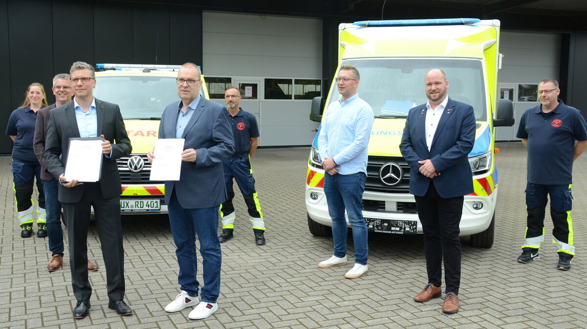 Landrat Thorsten Krüger (r. vorne) und Dezernent Michael Take präsentieren die Exemplare des neuen Tarifvertrages für den Rettungsdienst vor den beiden neuen Einsatzfahrzeugen in Dorum. Für die Politik dabei: Thorsten Ohlandt und Hendrik Rehm, außerdem die Mitarbeiter Claudia Ehler, Stephan Romag und Malte Ahrens sowie Tim Brockmeyer, beim Landkreis zuständig für den Rettungsdienst. Foto: Rohde