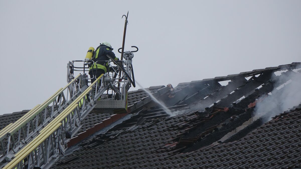 Eine Stunde nach Beginn der Löscharbeiten schlägt immer noch dichter Rauch aus dem Dach. Von beiden Seiten des Daches entfernen die Feuerwehrleute mit einem Einreißhaken (lange Lanze) die Dachziegel. Foto: Fischer