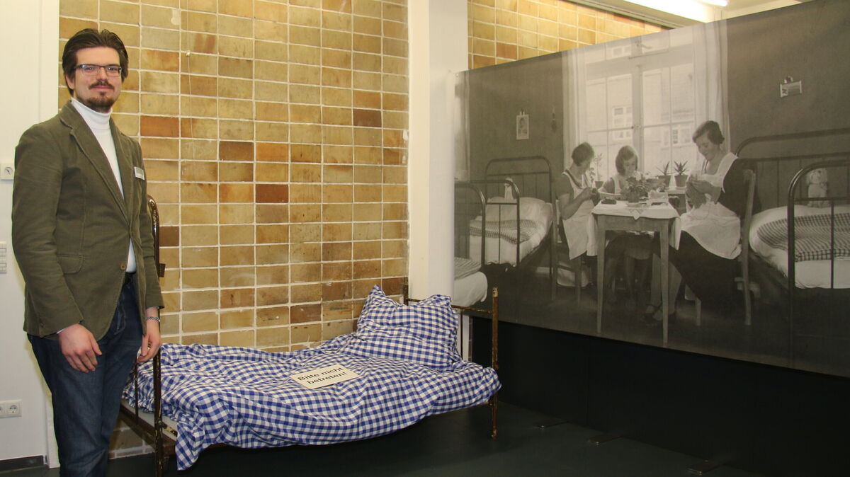 Ausstellungsmacher Philipp Roll vor einem der schmalen Betten, wie sie im Frauenwohnheim am Elfenweg standen. Zu viert teilten sich die Arbeiterinnen ein Zimmer, mit nicht viel mehr als einem Koffer als persönlichem Besitz. Foto: Potschka