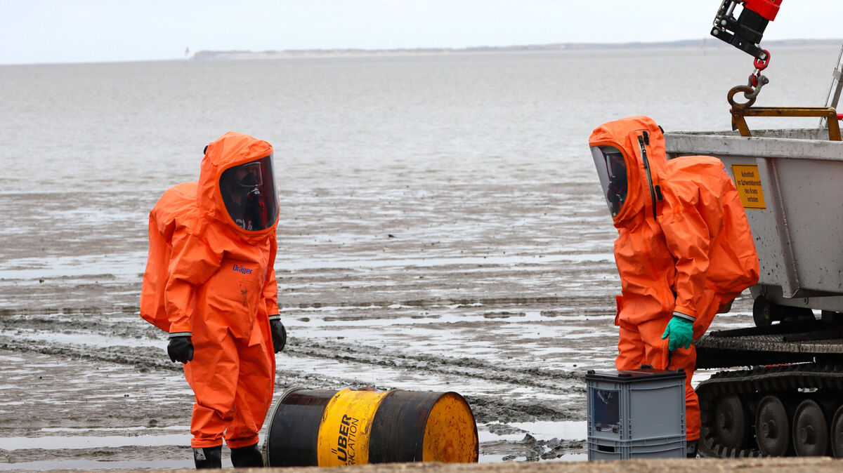 Zwei Feuerwehrleute aus der Gefahrguteinheit des Landkreises Wittmund untersuchen in schweren Schutzanzügen ein Chemie-Fass im Watt. Niklas Mock THW
