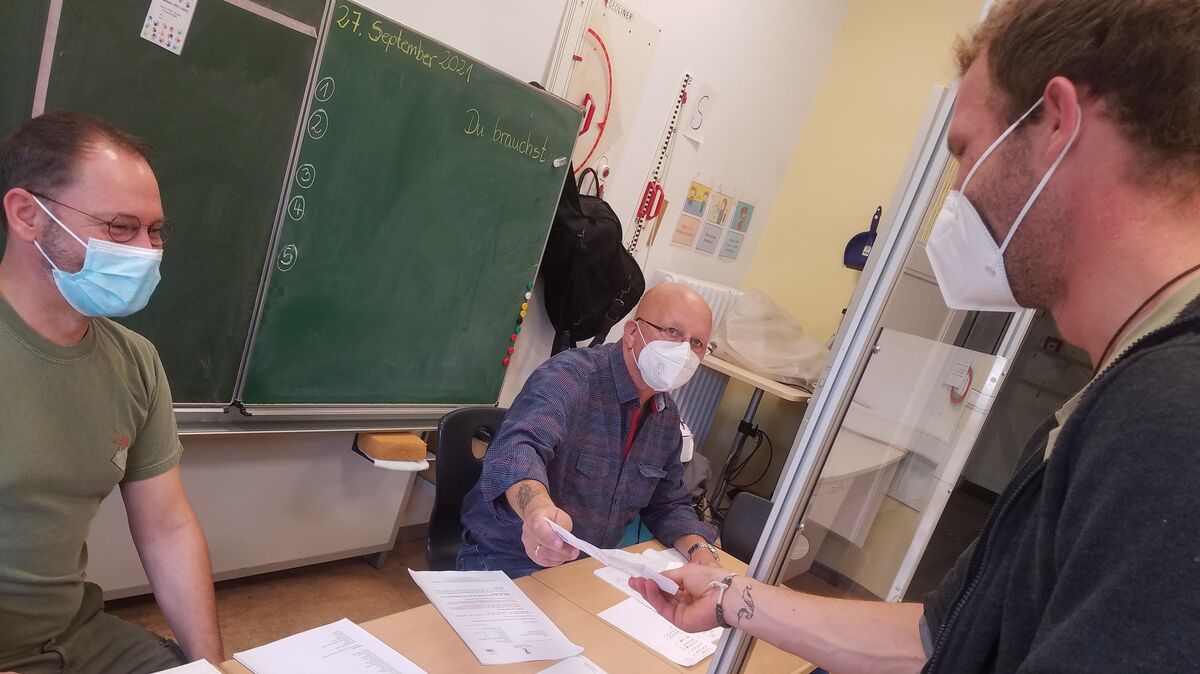 Lars-Günther Brandt nimmt in einem zum Wahllokal umfunktionierten Klassenzimmer der Cuxhavener Bleickenschule einen Wahlschein von Kilian Evert entgegen. Foto: Käfer