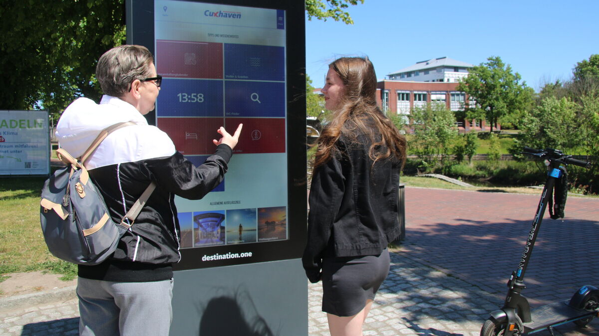 Oma und Enkelin informieren sich an der neuen Info-Stele bei der „Hermine“ über Veranstaltungen in Cuxhaven – trotz technischer Kinderkrankheiten ein beliebter digitaler Wegweiser. Foto: Potschka