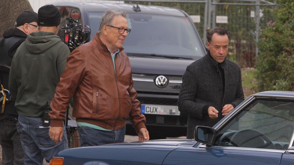 Hansjürgen Hürrig (l.) und Jan Josef Liefers kommen aus der Rundturnhalle. Im Hintergrund sind die Kameraleute zu sehen. Mehrere Fahrzeuge aus dem Fuhrpark haben ein Cuxhavener Kennzeichen. Foto: FoTe Press Matthias Röhe